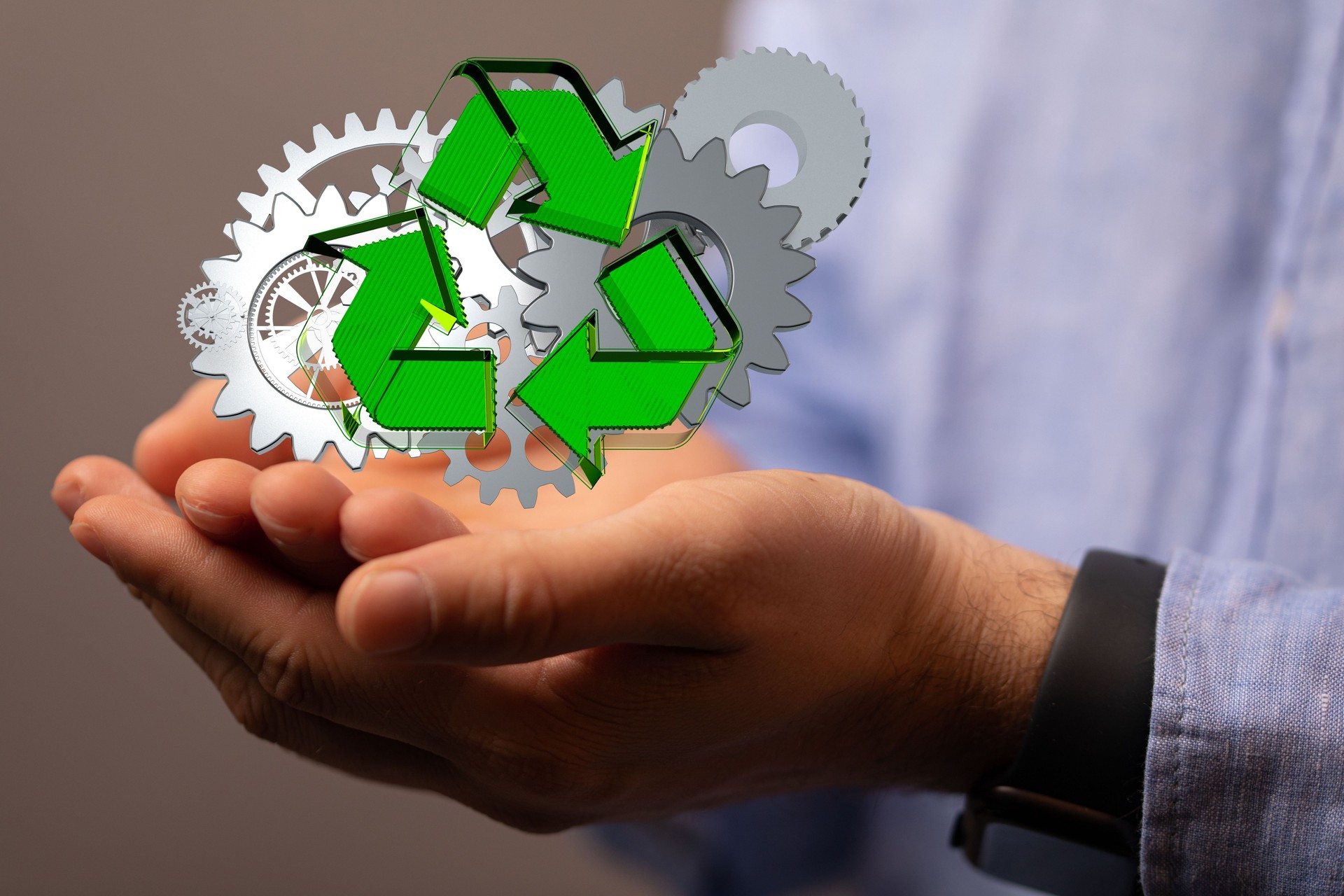 Person holding an illustrative recycle symbol and gears in his hands.